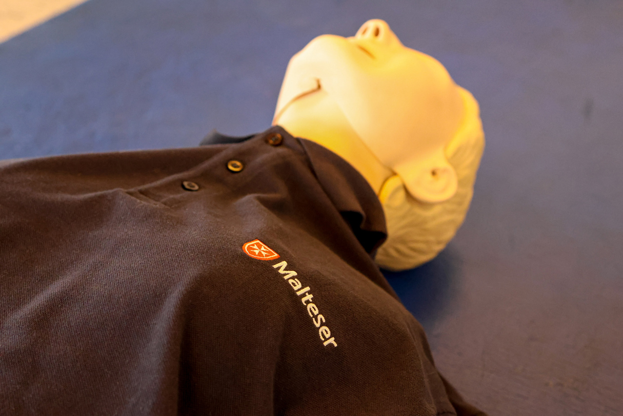 Übungspuppe für Erste-Hilfe-Kurse, bekleidet mit einem Malteser-Poloshirt.